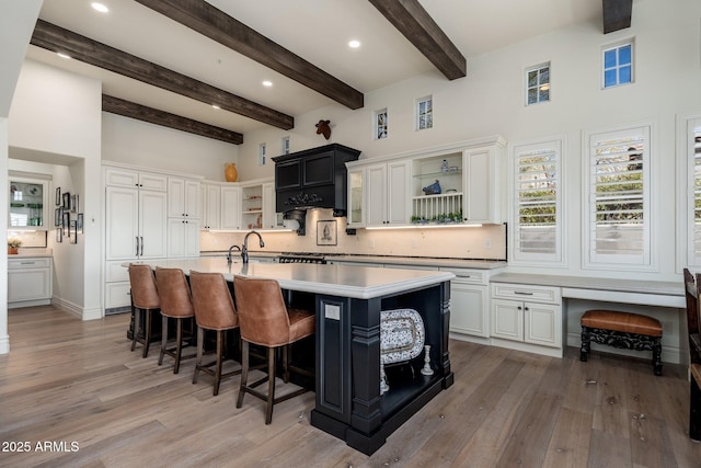 kitchen featuring open shelves, light countertops, backsplash, and a center island with sink