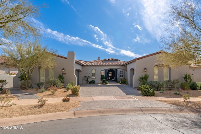 mediterranean / spanish home with a garage, a tiled roof, decorative driveway, and stucco siding