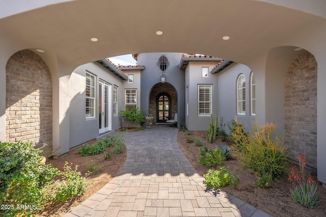 view of exterior entry with french doors, brick siding, and stucco siding