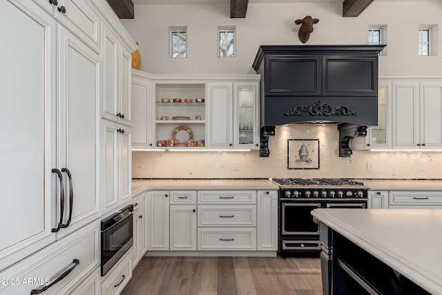 kitchen with light countertops, white cabinetry, built in microwave, double oven range, and premium range hood