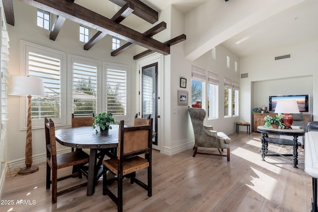 dining area with light wood-style flooring, a high ceiling, visible vents, baseboards, and beamed ceiling