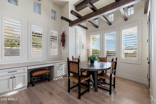 dining area featuring built in desk, beamed ceiling, light wood-style flooring, and baseboards