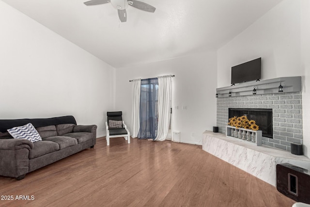 living room with vaulted ceiling, wood-type flooring, a brick fireplace, and ceiling fan