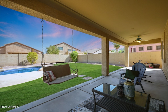 patio terrace at dusk with ceiling fan, a fenced in pool, and a lawn