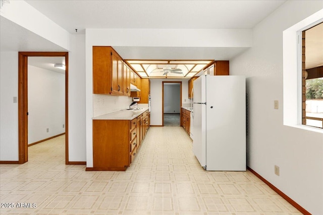 kitchen with light countertops, freestanding refrigerator, brown cabinets, and baseboards