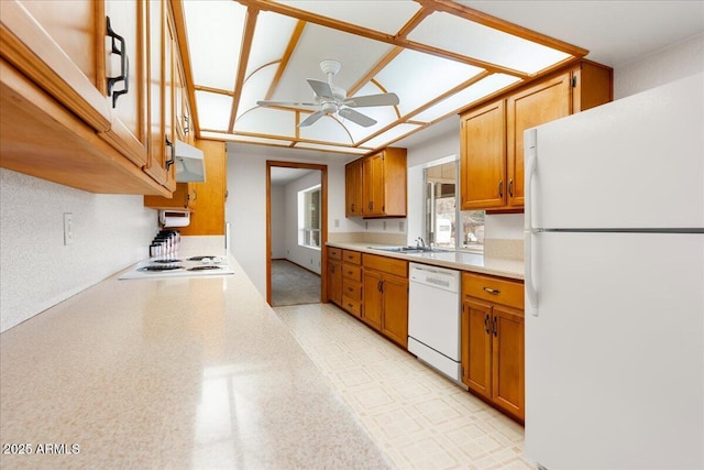 kitchen with brown cabinets, light countertops, a sink, ceiling fan, and white appliances