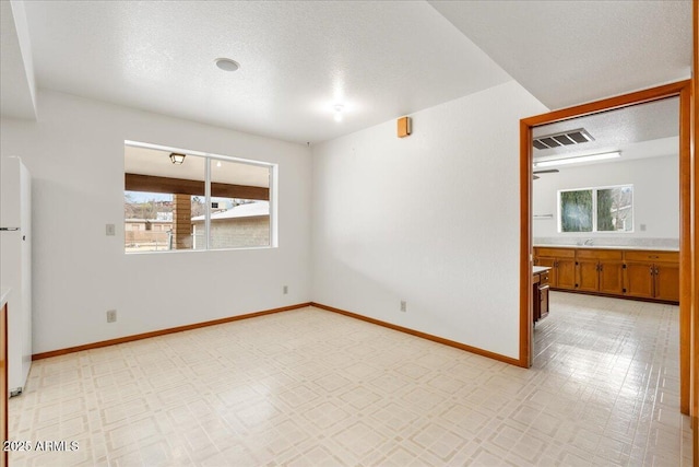 spare room featuring a textured ceiling, light floors, visible vents, and baseboards