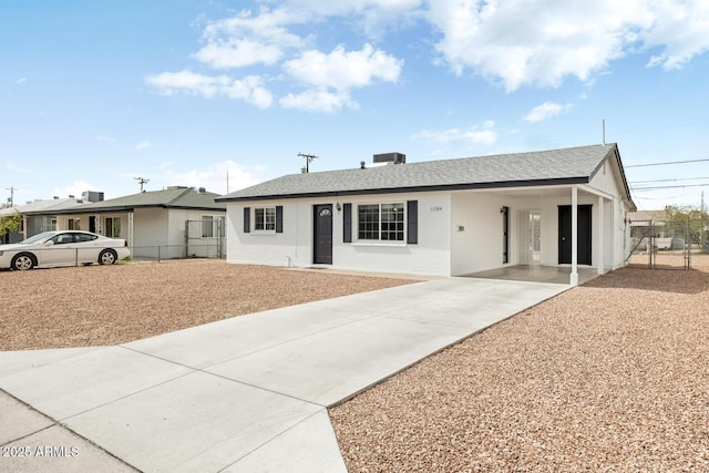 ranch-style house featuring an attached carport, roof with shingles, concrete driveway, and fence