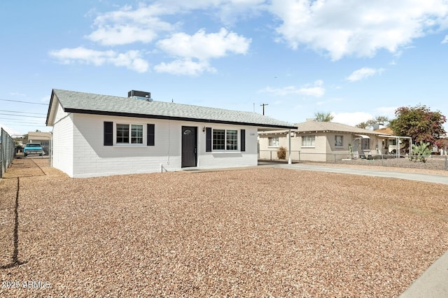 single story home with concrete block siding, an attached carport, fence, driveway, and roof with shingles