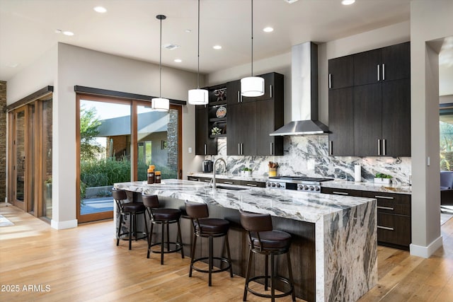 kitchen featuring wall chimney exhaust hood, a breakfast bar, tasteful backsplash, decorative light fixtures, and an island with sink