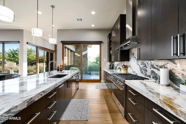 kitchen featuring sink, wall chimney range hood, backsplash, stainless steel appliances, and decorative light fixtures