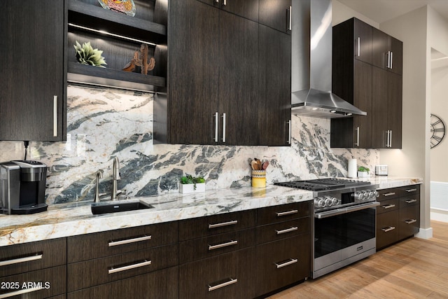 kitchen with tasteful backsplash, sink, stainless steel range, wall chimney exhaust hood, and light hardwood / wood-style flooring