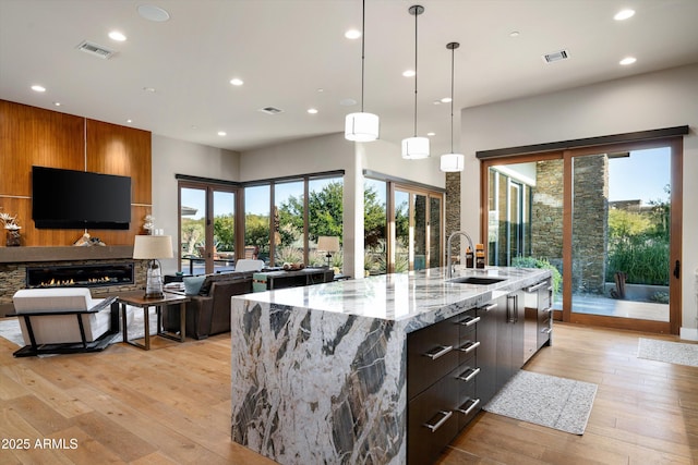 kitchen with sink, a large island with sink, hanging light fixtures, light stone counters, and light hardwood / wood-style flooring