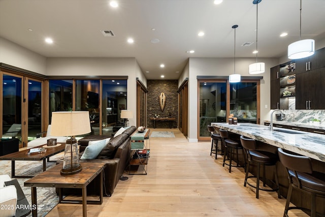 kitchen featuring sink, light hardwood / wood-style flooring, hanging light fixtures, dark brown cabinets, and light stone countertops