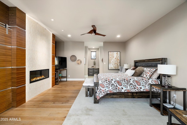 bedroom with light hardwood / wood-style floors, a large fireplace, and ceiling fan