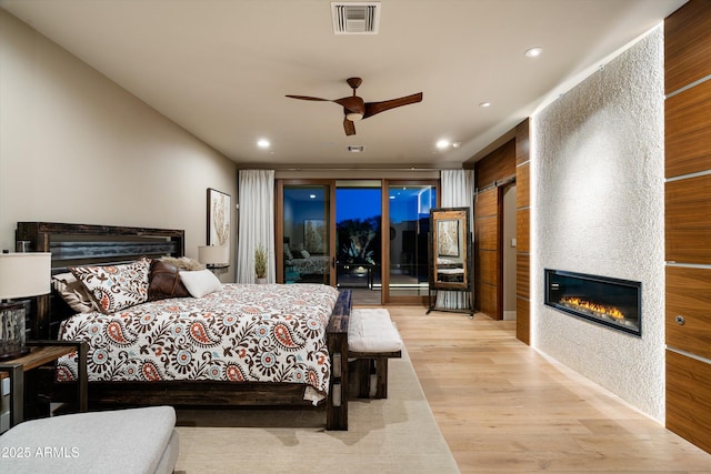 bedroom with a fireplace, access to outside, light hardwood / wood-style floors, and ceiling fan