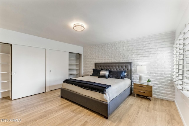 bedroom featuring brick wall, light wood-type flooring, and two closets