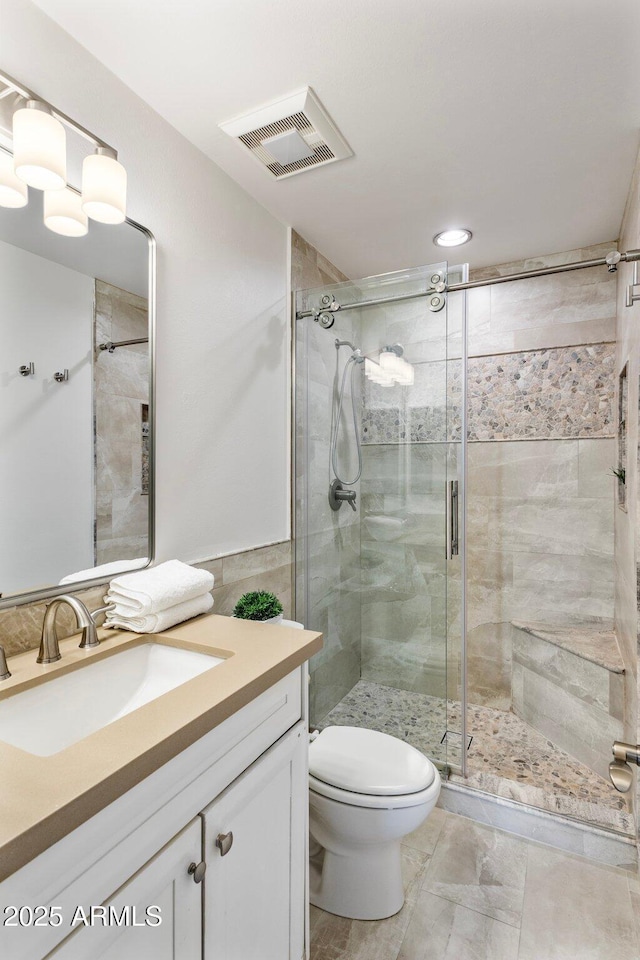 bathroom with a stall shower, visible vents, vanity, and toilet