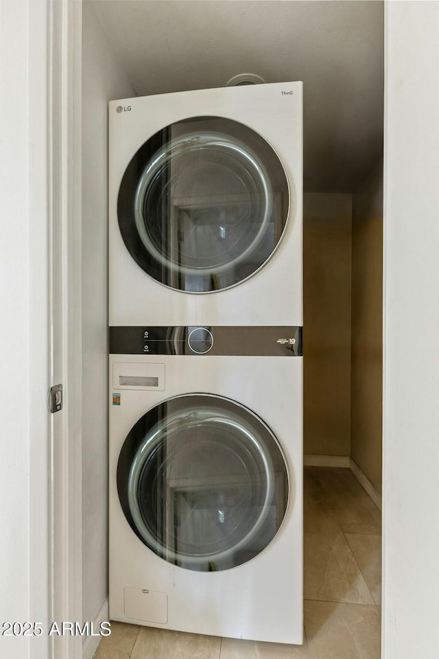 laundry area with stacked washer and dryer, tile patterned flooring, laundry area, and baseboards