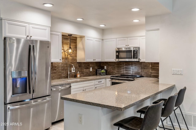 kitchen with a peninsula, appliances with stainless steel finishes, a sink, and white cabinets