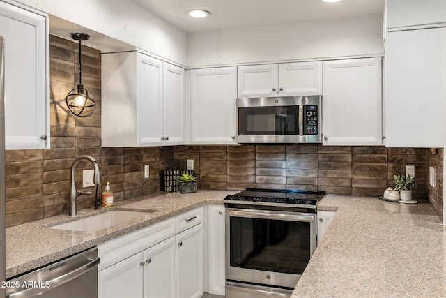 kitchen featuring light stone counters, stainless steel appliances, a sink, white cabinetry, and decorative backsplash