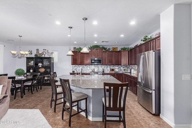 kitchen with appliances with stainless steel finishes, pendant lighting, an island with sink, and a notable chandelier