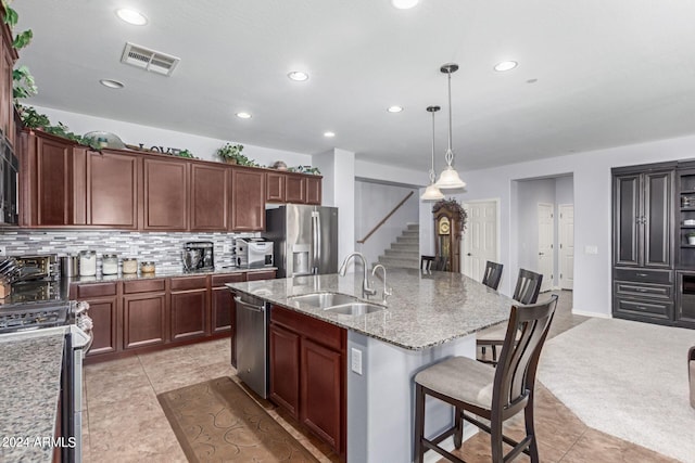 kitchen with sink, an island with sink, a kitchen bar, appliances with stainless steel finishes, and decorative light fixtures