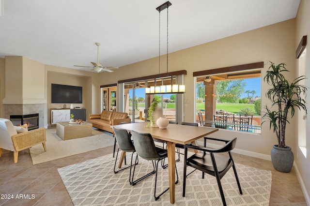 tiled dining room with a fireplace, a healthy amount of sunlight, and ceiling fan