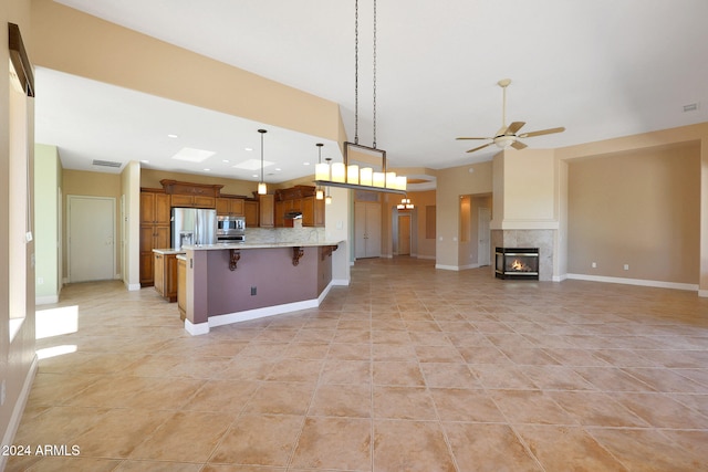 kitchen featuring a breakfast bar area, stainless steel appliances, pendant lighting, a fireplace, and tasteful backsplash