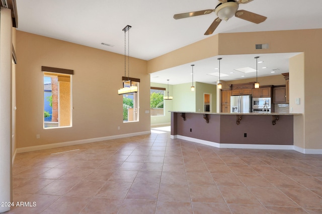 interior space featuring appliances with stainless steel finishes, kitchen peninsula, a kitchen breakfast bar, decorative light fixtures, and light stone counters