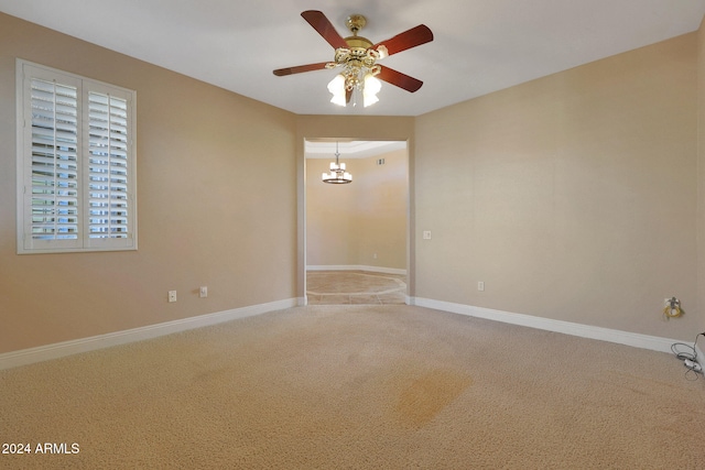 carpeted empty room featuring ceiling fan with notable chandelier