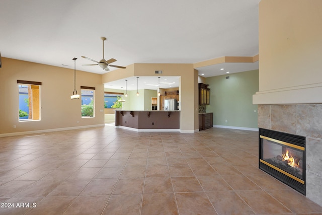 unfurnished living room with a tiled fireplace, light tile patterned floors, and ceiling fan