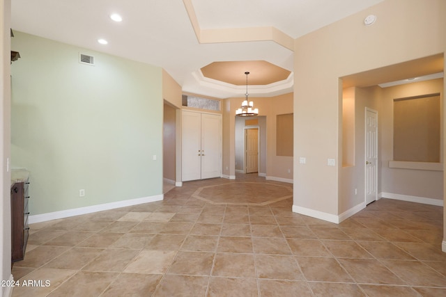 tiled spare room with a chandelier and a raised ceiling