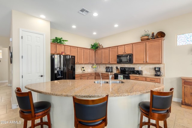 kitchen with a kitchen breakfast bar, sink, a center island with sink, and black appliances