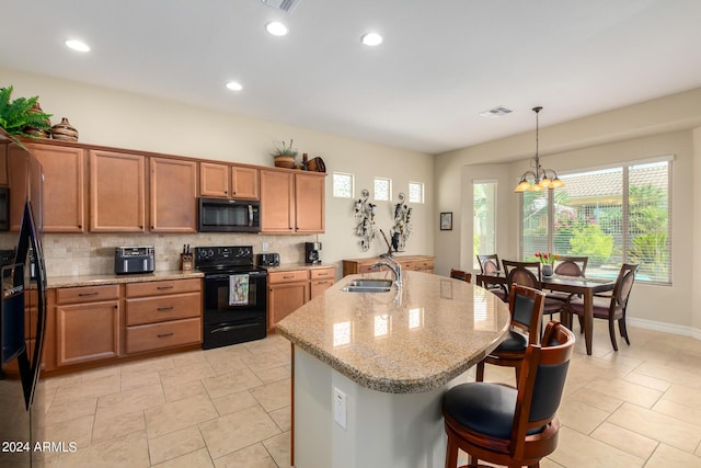 kitchen featuring sink, black appliances, decorative light fixtures, an inviting chandelier, and an island with sink