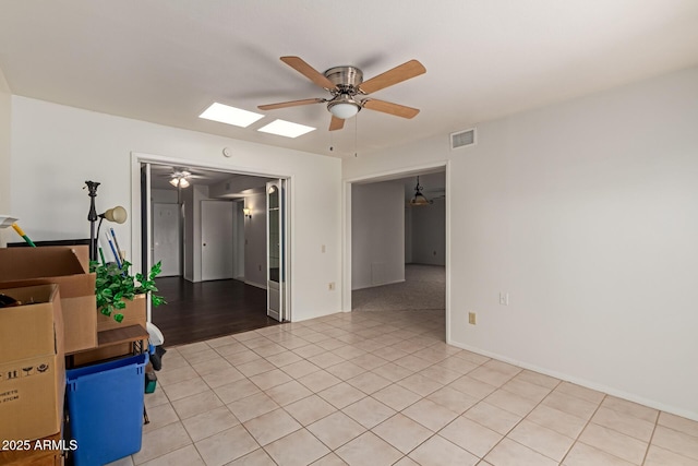 spare room featuring a skylight, light tile patterned floors, visible vents, and ceiling fan