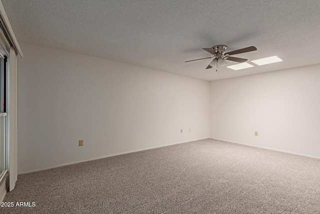 carpeted empty room featuring baseboards, a textured ceiling, a skylight, and a ceiling fan