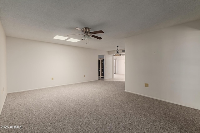 carpeted spare room with visible vents, a textured ceiling, a skylight, baseboards, and ceiling fan