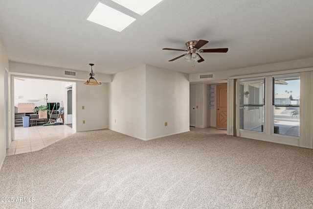 unfurnished room with visible vents, a ceiling fan, a skylight, and carpet flooring