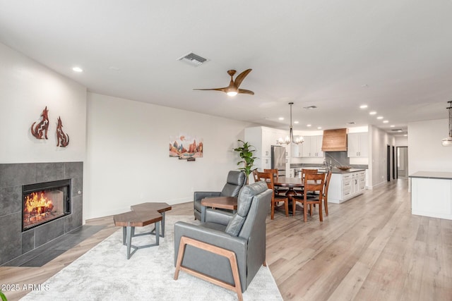 living room with ceiling fan with notable chandelier, a fireplace, and light hardwood / wood-style floors