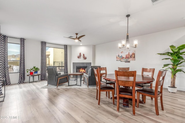 dining space with ceiling fan with notable chandelier, a premium fireplace, and light hardwood / wood-style floors