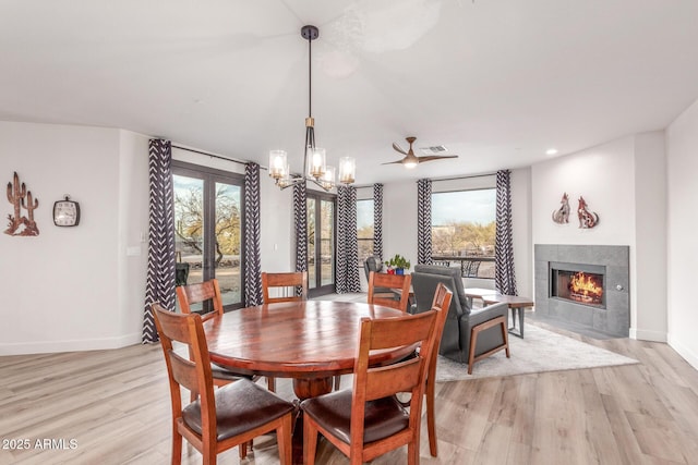 dining room featuring an inviting chandelier, light hardwood / wood-style flooring, a tile fireplace, and french doors