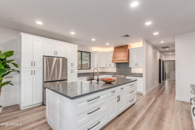 kitchen featuring light hardwood / wood-style flooring, premium range hood, backsplash, an island with sink, and white cabinets