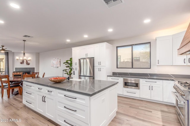 kitchen with appliances with stainless steel finishes, pendant lighting, white cabinets, light hardwood / wood-style floors, and a center island with sink