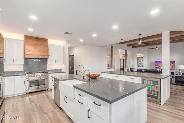 kitchen featuring premium range hood, appliances with stainless steel finishes, sink, white cabinets, and a center island with sink