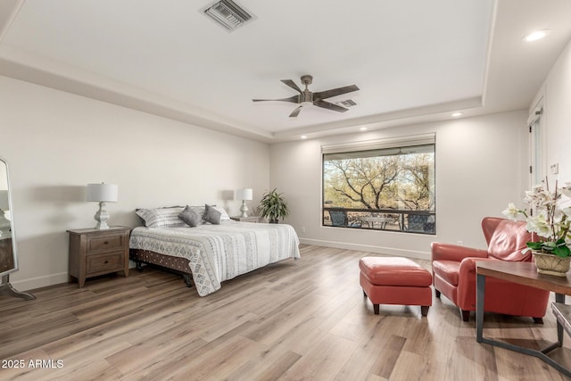 bedroom with ceiling fan, wood-type flooring, and a raised ceiling