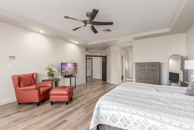 bedroom with ceiling fan, a tray ceiling, and light wood-type flooring