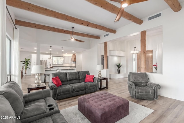 living room with beamed ceiling, ceiling fan with notable chandelier, and light wood-type flooring