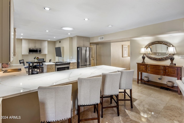 kitchen featuring light stone countertops, sink, kitchen peninsula, stainless steel appliances, and a breakfast bar area