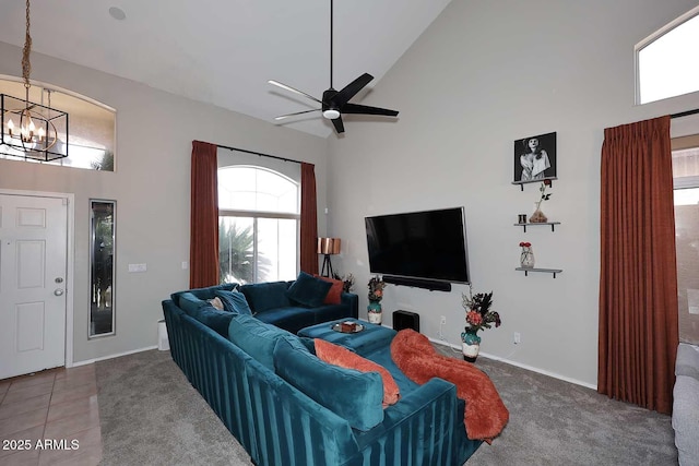 carpeted living area featuring ceiling fan with notable chandelier, high vaulted ceiling, tile patterned flooring, and baseboards